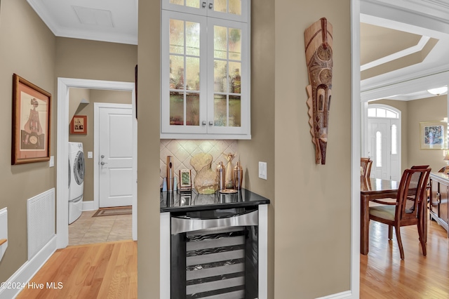 bar with white cabinetry, tasteful backsplash, wine cooler, washer / dryer, and light wood-type flooring