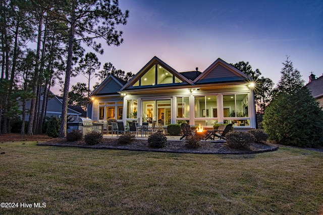 back house at dusk featuring a yard, a patio, an outdoor fire pit, and a sunroom