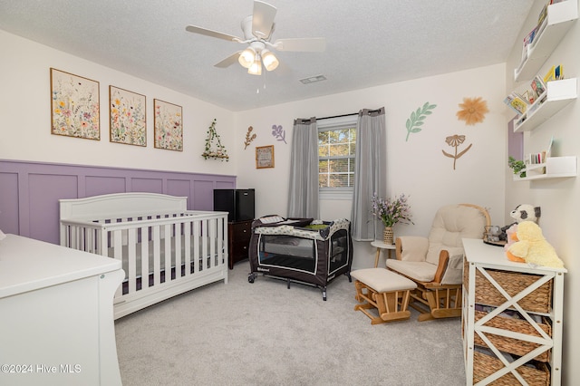 bedroom with a textured ceiling, carpet floors, a nursery area, and ceiling fan