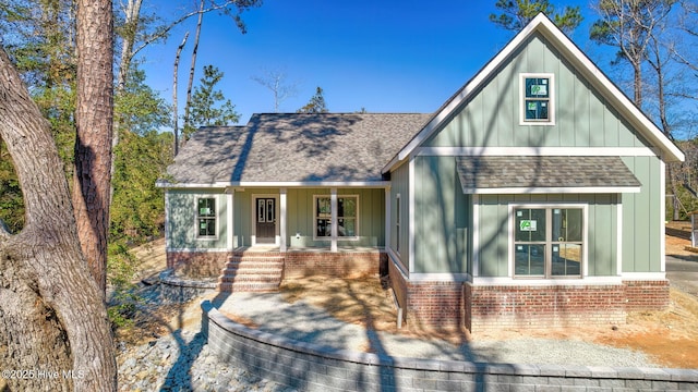 view of front of property with a shingled roof, a porch, board and batten siding, and brick siding