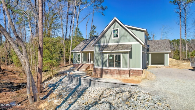 view of front facade featuring gravel driveway, roof with shingles, and brick siding