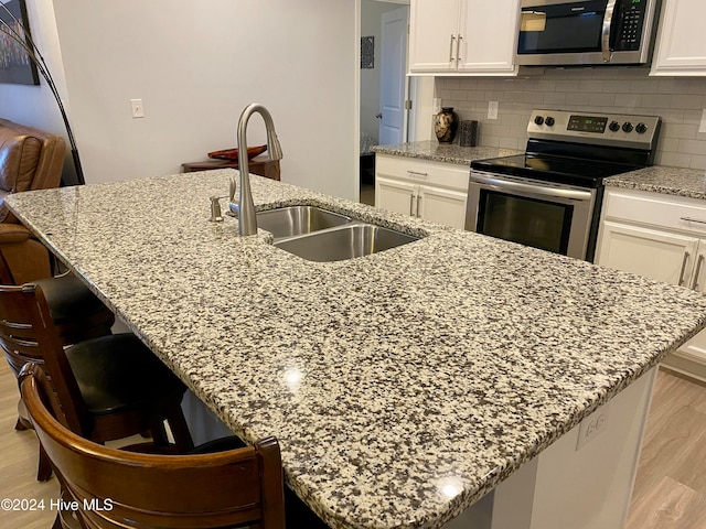 kitchen with a breakfast bar, a kitchen island with sink, sink, light hardwood / wood-style flooring, and appliances with stainless steel finishes