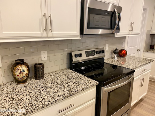 kitchen featuring decorative backsplash, light stone countertops, light hardwood / wood-style floors, white cabinetry, and stainless steel appliances