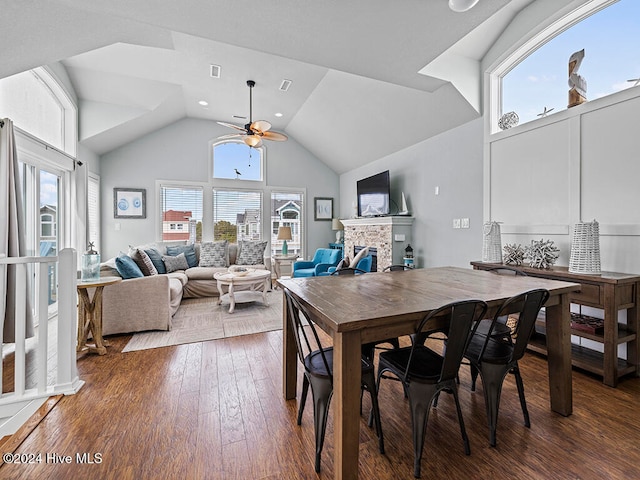 dining room featuring a stone fireplace, ceiling fan, hardwood / wood-style floors, and high vaulted ceiling