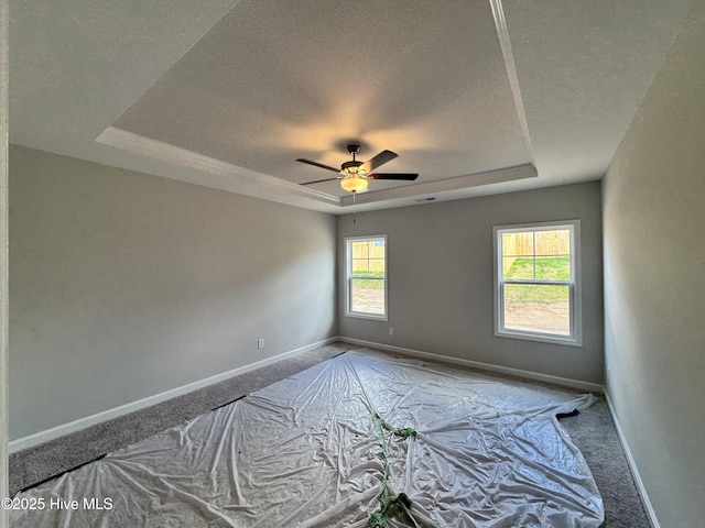 carpeted empty room with a ceiling fan, a textured ceiling, baseboards, and a raised ceiling