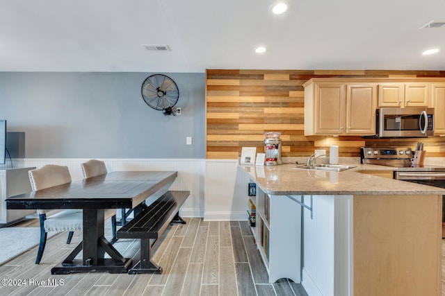 kitchen with sink, light stone counters, hardwood / wood-style floors, wooden walls, and appliances with stainless steel finishes