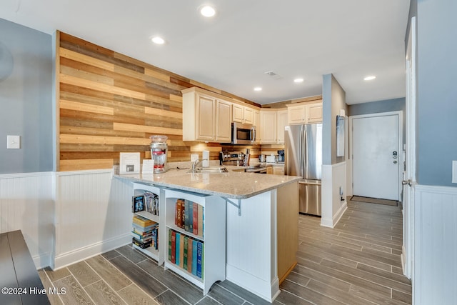 kitchen with sink, light stone countertops, appliances with stainless steel finishes, kitchen peninsula, and a breakfast bar area