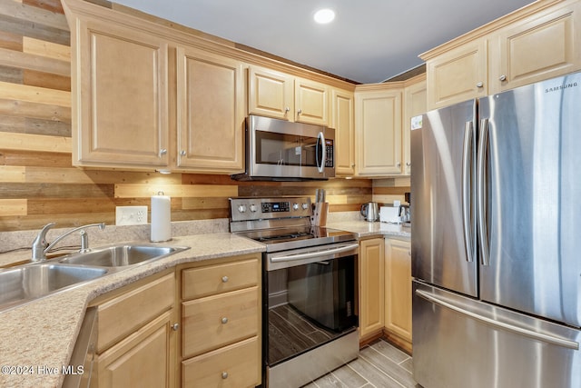 kitchen featuring wood walls, sink, light hardwood / wood-style flooring, light stone counters, and stainless steel appliances