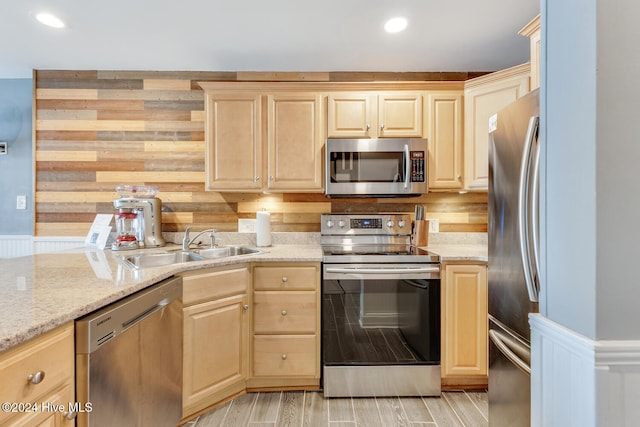 kitchen with light stone countertops, stainless steel appliances, sink, light brown cabinets, and light hardwood / wood-style flooring