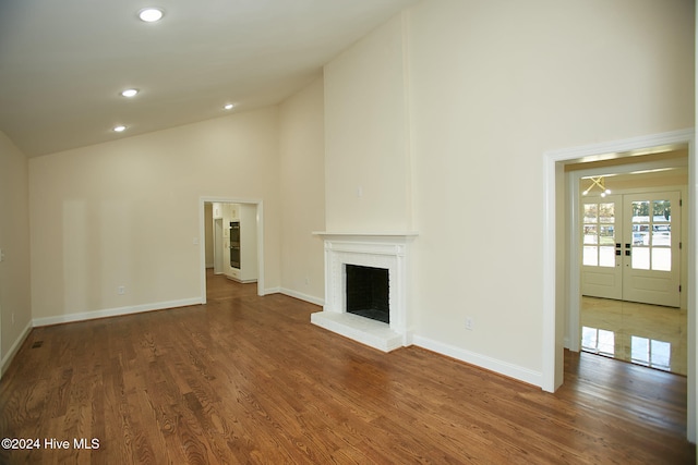 unfurnished living room with dark hardwood / wood-style flooring, high vaulted ceiling, and french doors