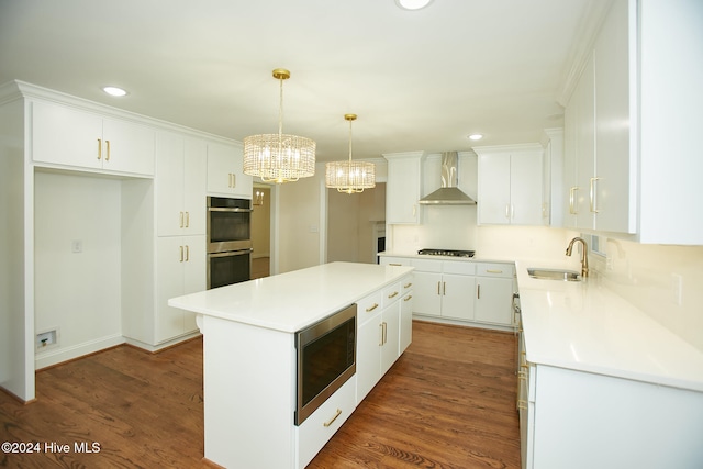 kitchen with stainless steel appliances, sink, wall chimney range hood, a center island, and white cabinetry