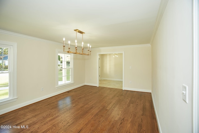 empty room featuring wood-type flooring, crown molding, a wealth of natural light, and an inviting chandelier