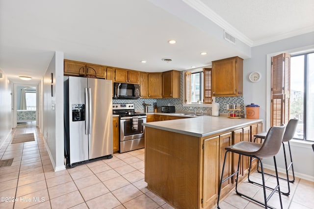 kitchen with kitchen peninsula, appliances with stainless steel finishes, a breakfast bar area, light tile patterned floors, and ornamental molding