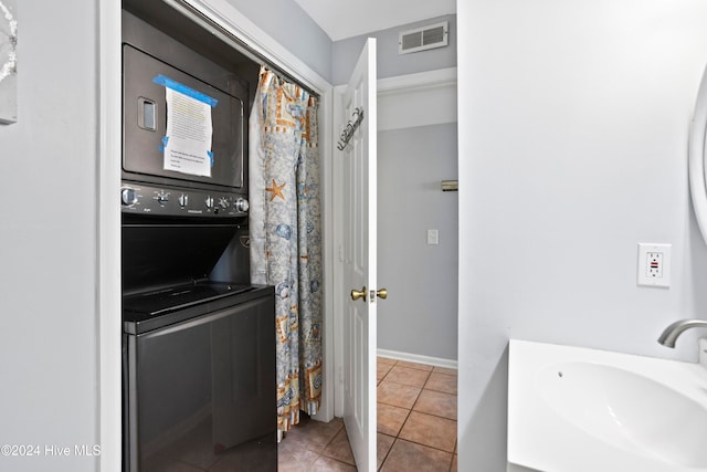 laundry area featuring sink, light tile patterned floors, and stacked washer and clothes dryer