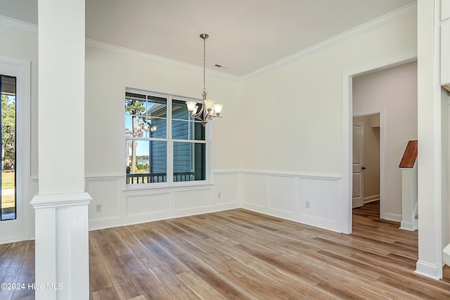 unfurnished dining area featuring a notable chandelier, light wood-type flooring, ornamental molding, and ornate columns