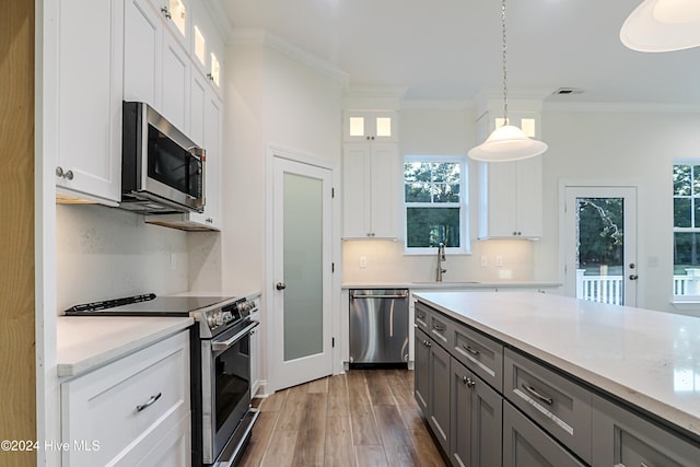 kitchen featuring crown molding, appliances with stainless steel finishes, decorative light fixtures, dark hardwood / wood-style flooring, and white cabinetry