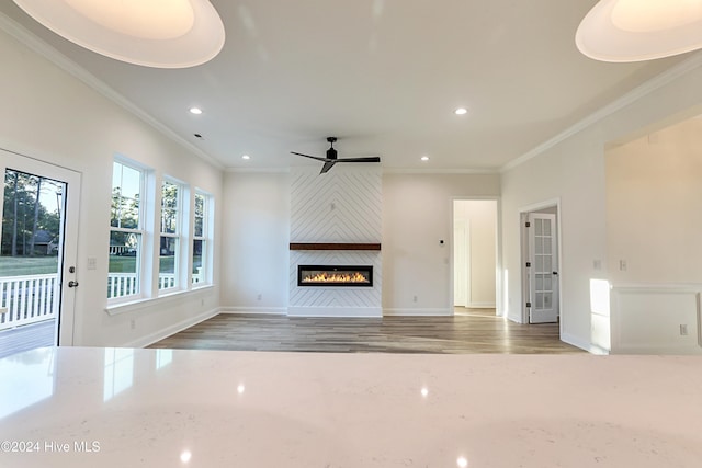 unfurnished living room featuring ceiling fan, a fireplace, wood-type flooring, and ornamental molding