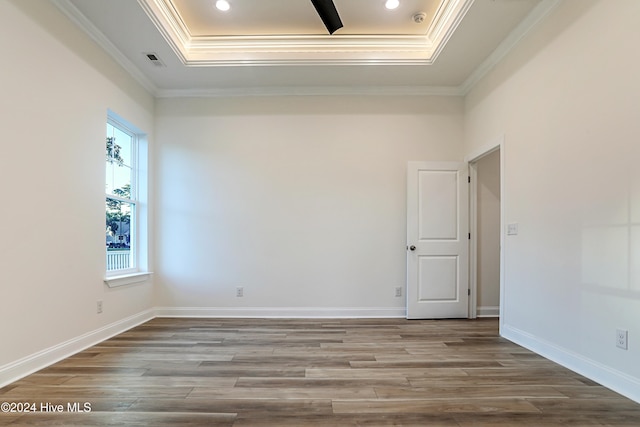 empty room with wood-type flooring, a tray ceiling, and crown molding