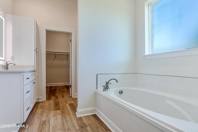 bathroom with hardwood / wood-style flooring, vanity, and a relaxing tiled tub