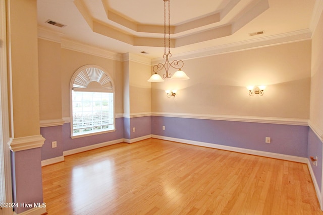 empty room featuring wood-type flooring, crown molding, a tray ceiling, and a chandelier