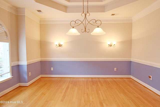 empty room featuring a raised ceiling, wood-type flooring, and ornamental molding