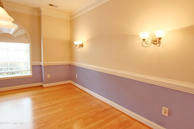 spare room with wood-type flooring, ornamental molding, and a chandelier