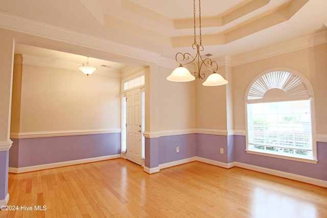 empty room with a tray ceiling, crown molding, hardwood / wood-style floors, and an inviting chandelier