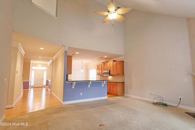 unfurnished living room featuring ceiling fan, a towering ceiling, ornamental molding, and light wood-type flooring