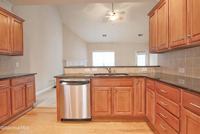 kitchen featuring stainless steel dishwasher, light hardwood / wood-style floors, dark stone countertops, and sink