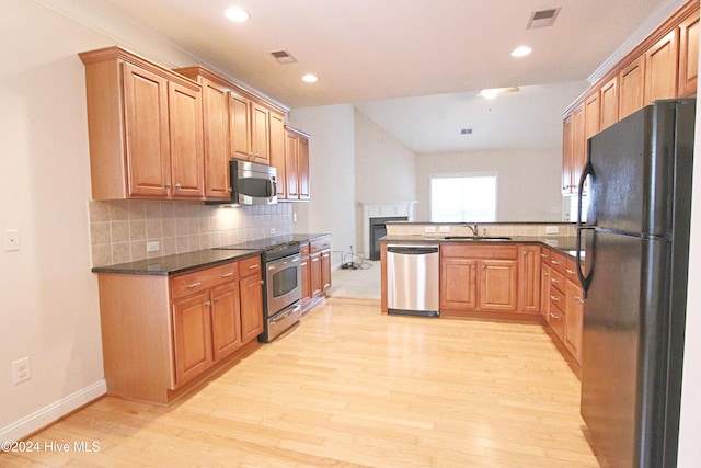 kitchen with dark stone counters, stainless steel appliances, light hardwood / wood-style floors, and sink