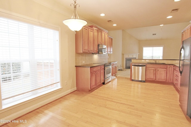 kitchen with appliances with stainless steel finishes, tasteful backsplash, sink, pendant lighting, and light hardwood / wood-style flooring