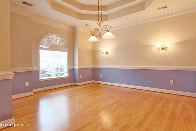 empty room featuring wood-type flooring, ornamental molding, a tray ceiling, and an inviting chandelier