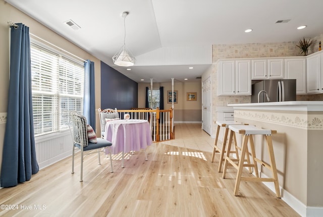 kitchen with lofted ceiling, white cabinets, hanging light fixtures, stainless steel fridge, and light wood-type flooring