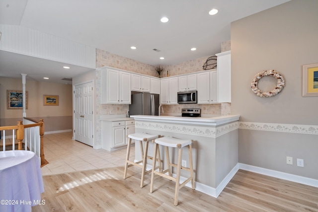 kitchen featuring stainless steel appliances, a kitchen breakfast bar, kitchen peninsula, light hardwood / wood-style floors, and white cabinets