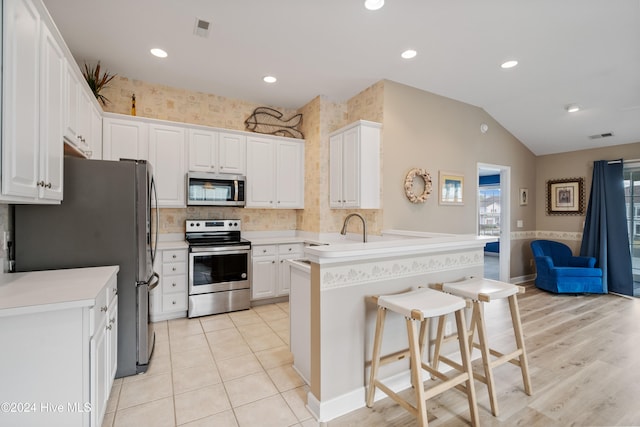 kitchen with kitchen peninsula, appliances with stainless steel finishes, a breakfast bar, and white cabinets