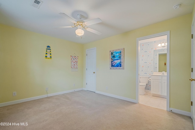 unfurnished bedroom with ceiling fan, ensuite bathroom, and light colored carpet