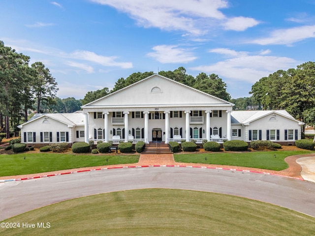 greek revival house featuring covered porch and a front yard