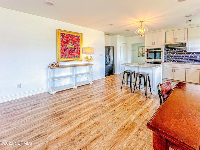 kitchen with a kitchen bar, black appliances, decorative light fixtures, a center island, and white cabinetry