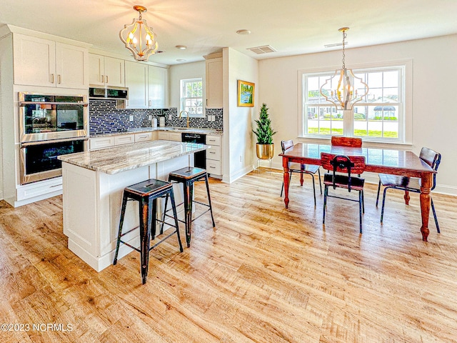 kitchen featuring white cabinetry, light stone countertops, an inviting chandelier, a kitchen island, and light wood-type flooring