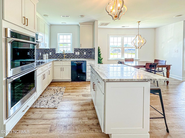 kitchen with stainless steel appliances, decorative light fixtures, an inviting chandelier, a center island, and light hardwood / wood-style floors