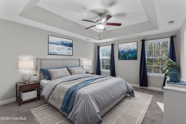 carpeted bedroom featuring ceiling fan and a raised ceiling