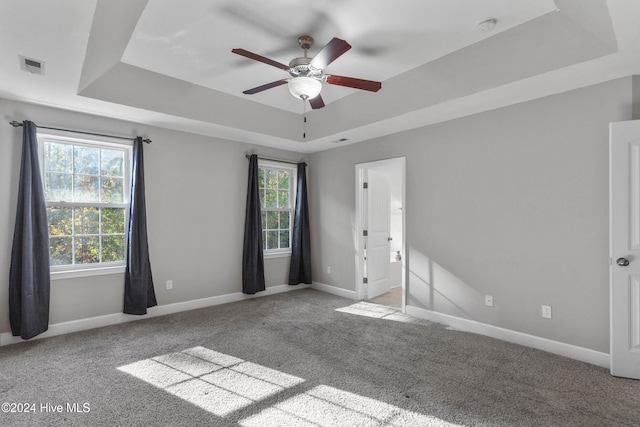 carpeted empty room featuring ceiling fan and a raised ceiling