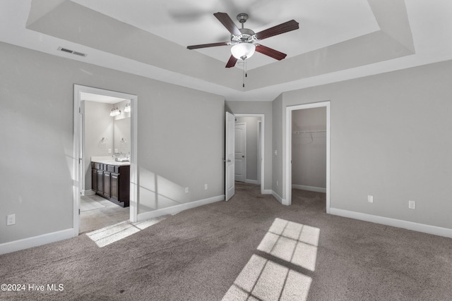 unfurnished bedroom with ceiling fan, a raised ceiling, light colored carpet, and ensuite bath