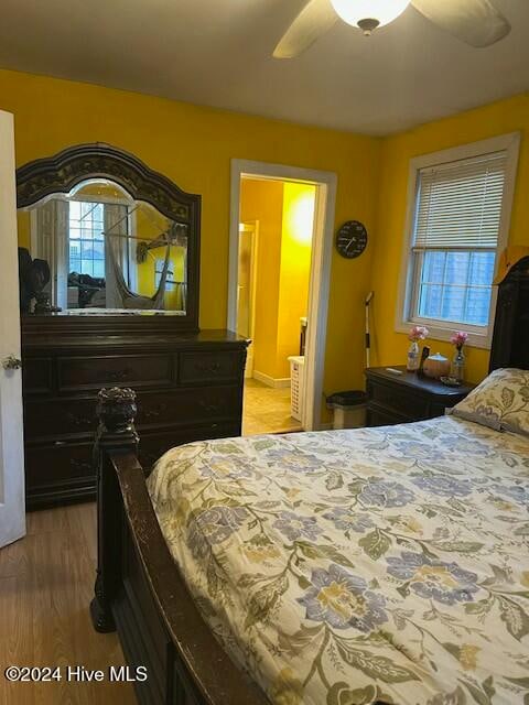 bedroom featuring ensuite bathroom, hardwood / wood-style flooring, multiple windows, and ceiling fan