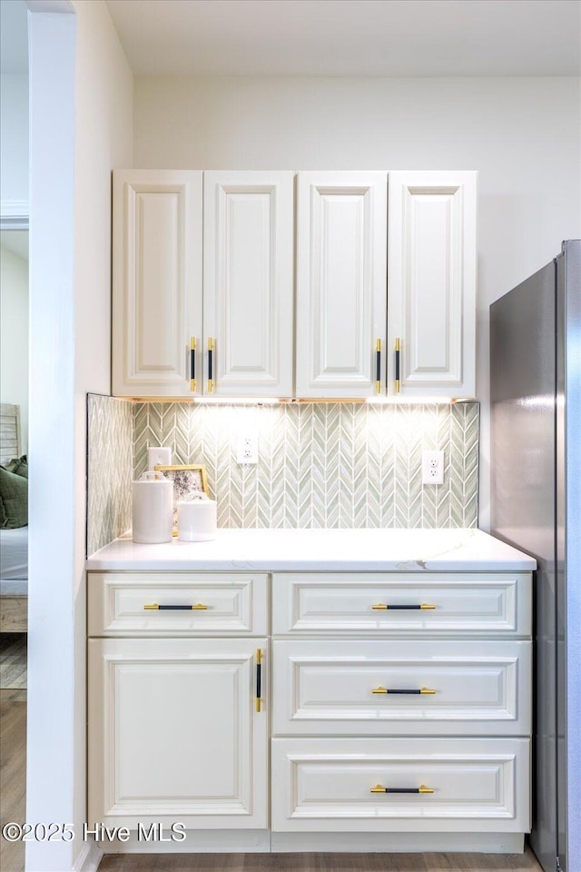 bar with decorative backsplash, white cabinetry, and stainless steel refrigerator