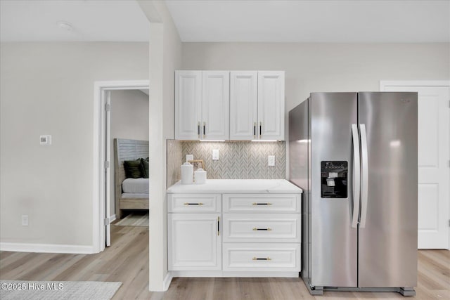 kitchen featuring white cabinets, decorative backsplash, stainless steel fridge, and light wood-type flooring