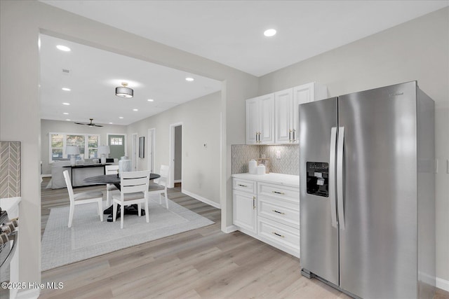 kitchen with backsplash, white cabinets, ceiling fan, stainless steel fridge, and light hardwood / wood-style floors