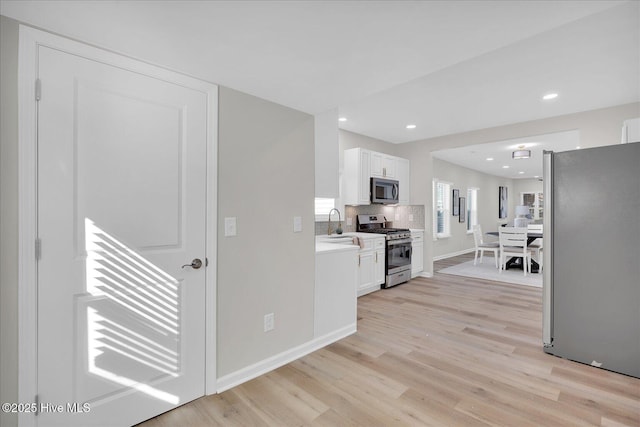 kitchen featuring decorative backsplash, stainless steel appliances, sink, light hardwood / wood-style floors, and white cabinetry