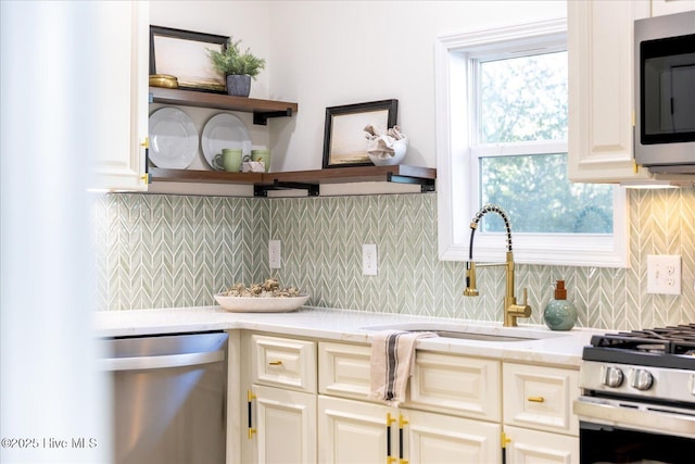 kitchen with sink, stainless steel appliances, light stone counters, backsplash, and cream cabinets