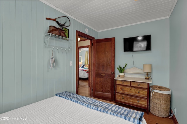 bedroom with hardwood / wood-style flooring, wood walls, and ornamental molding